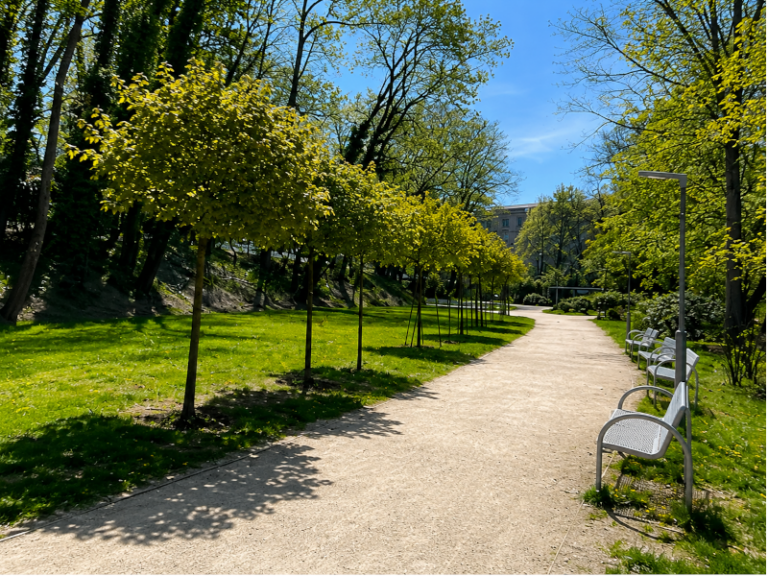 Park u Krajského úřadu Libereckého kraje v Liberci se světlou cestou, lavičkami a jarní zelení.